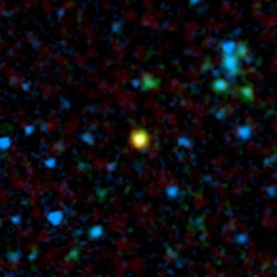 In this artificially colored image taken by the Spitzer Space Telescope we see a distant galaxy (in yellow) containing a quasar - a supermassive black hole surrounded by a ring or bulge of gas and dust.