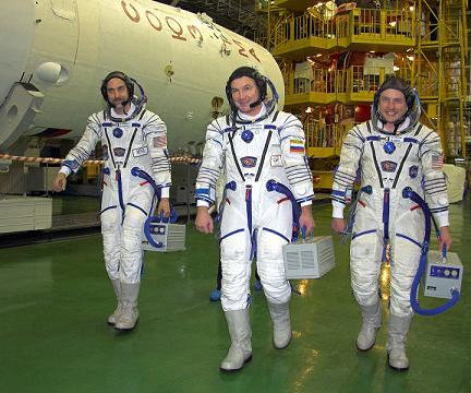 בתמונה משמאל: ריצ'ארד גאריוט, יורי לונצ'קוב ומייקל פיניקי הולכים לחללית סויוז TMA-13 לצורך מדידת חליפות החלל במתקן ההרכבה בבייקונור