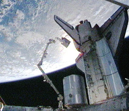 בתמונה: האסטרונאוט כריס פוגלסאנג רוכב על גבי הזרוע הרובוטית של התחנה כשהוא נושא מכל אמוניה ריק לאיחסון בסיפון המטען של המעבורת. צילום: הטלוויזיה של נאס''א