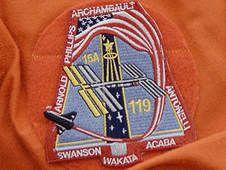 תג משימה STS-119 ועליו מודגשים קולטי השמש החדשים שהמעבורת מעלה איתה לתחנה
