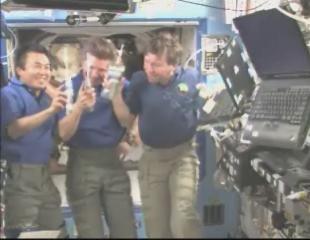 Space station crew members raise glasses of water as they chat with the Atlantis astronauts who upgraded the Hubble Space Telescope