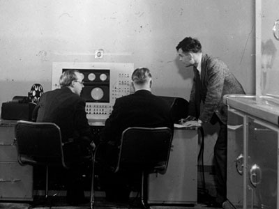אלן טיורינג (עומד מימין), בריאן פולארד וקית לונסדייל ליד פראנטי סימן 1, מחשב רב-תכליתי שהיה המחשב המסחרי השני. צילום: Courtesy of The University of Manchester, the School of Computer Science