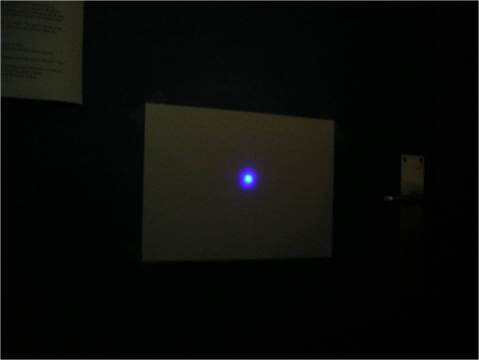 الصورة 4: شعاع ليزر بالأشعة تحت الحمراء يتم تحويله إلى شعاع ليزر أزرق باستخدام العملية الموضحة أعلاه ويتم عرضه على شاشة في غرفة مظلمة. مصدر الصورة: جيل.