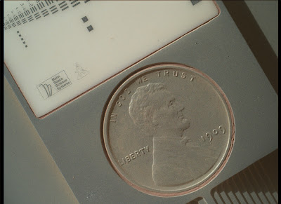 לוחית כיול למצלמת הזרוע, ועליה מטבע אמיתי של פני (1 סנט), שגודלו בערך כגודלו של שקל אחד. הגרגר שרואים בבירור מתחת לספרה 9 הוא בקוטר של עשירית מילימטר. 