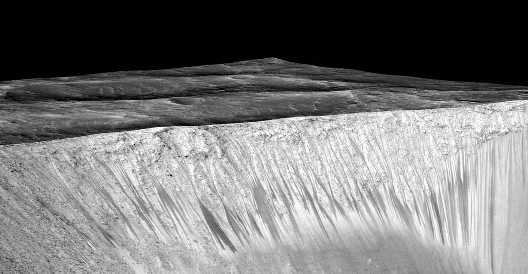 These dark, narrow channels called (SRL) recurring slope lineae emanate from the walls of Garni Crater on Mars. The dark channels here reach a length of hundreds of meters. It is hypothesized that they were formed by the flow of brackish water on Mars, as photographed by the MRO spacecraft. Credits: NASA/JPL/University of Arizona