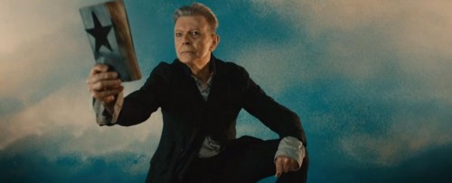 Image from the music video for the song Blackstar. David Bowie as a priest who offers a new religion, the Black Star book for the weird and the unusual.