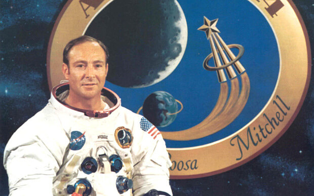 האסטרונאוט אדגר מיטשל בתמונה רשמית של נאס"א על רקע סמליל משימת אפולו 14