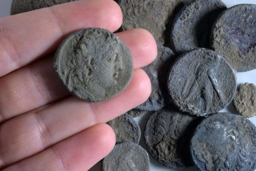 מטבע אנטיוכוס השביעי על רקע שאר מטבעות המטמון שנחשפו – צילום סטודיו: קלרה עמית