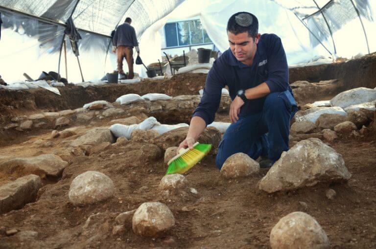 כפיר ארביב, מנהל החפירה מטעם רשות מהעתיקות, מנקה את אחת מאבני הקלע באתר החפירה במגרש הרוסים בו התגלה המקום ממנו צרו הרומאים על ירושלים. צילום: יולי שוורץ, באדיבות רשות העתיקות