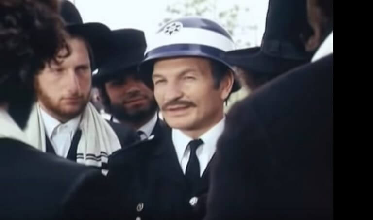 Sheika Ofir disperses an ultra-Orthodox demonstration in the role of policeman Avraham Azulai in the movie "The Policeman Azulai". He asks the ultra-Orthodox demonstrators when the Israelites sat in Sukkot precisely during Passover and they sing in response "Israel's Exodus from Egypt". Screenshot