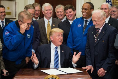 טראמפ חותם על הצו הנשיאותי ביום שישי. משמאלו, בחליפה, עומד האסטרונאוט באז אולדרין, האדם השני שהלך על הירח. שני האסטרונאוטים בחליפות כחולות הם אלוין דרו ודיוויד וולף. אסטרונאוטים נוספת, שלא נראית בתמונה אך נכחה בטקס, היא סנדרה מגנוס. צילום: NASA/Aubrey Gemignani.