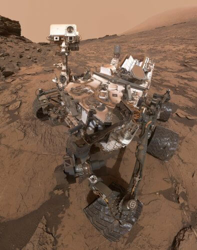 Curiosity in a "selfie" photo she took in 2016, which actually consists of several photos stitched together. Behind on the right you can see Mount Sharp, whose upper layers Curiosity is making its way to. Source: NASA.