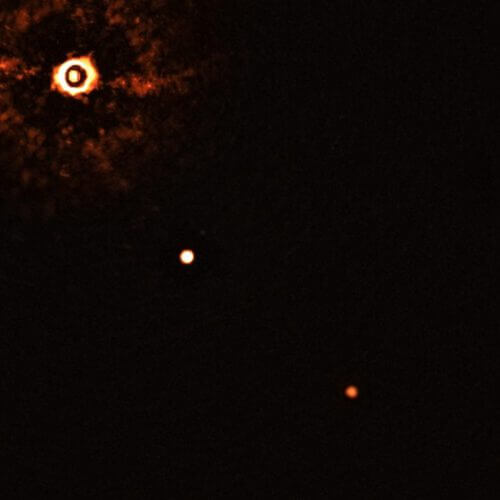 התמונה הזאת, שצולמה על ידי המכשיר SPHERE בטלסקופ הגדול מאוד של ESO, מראה את הכוכב TYC 8998-760-1 מלווה בשני כוכבי לכת חוץ שמשיים ענקיים. זאת הפעם הראשונה שאסטרונומים צפו ישירות ביותר מכוכב לכת אחד שמקיף כוכב הדומה לשמש. התמונה צולמה על ידי חסימת האור מהכוכב הצעיר הדומה לשמש (בפינה השמאלי עליונה) באמצעות קורונוגרף, שמאפשר גילוי של כוכבי לכת חלשים יותר. הטבעות הבהירות וכהות שרואים על דמות הכוכב הן מכשירים אופטיים. שני כוכבי הלכת נראים כשתי נקודות בהירות במרכז התמונה ובפינה הימנית תחתונה. מזכה: ESO/Bohn et al