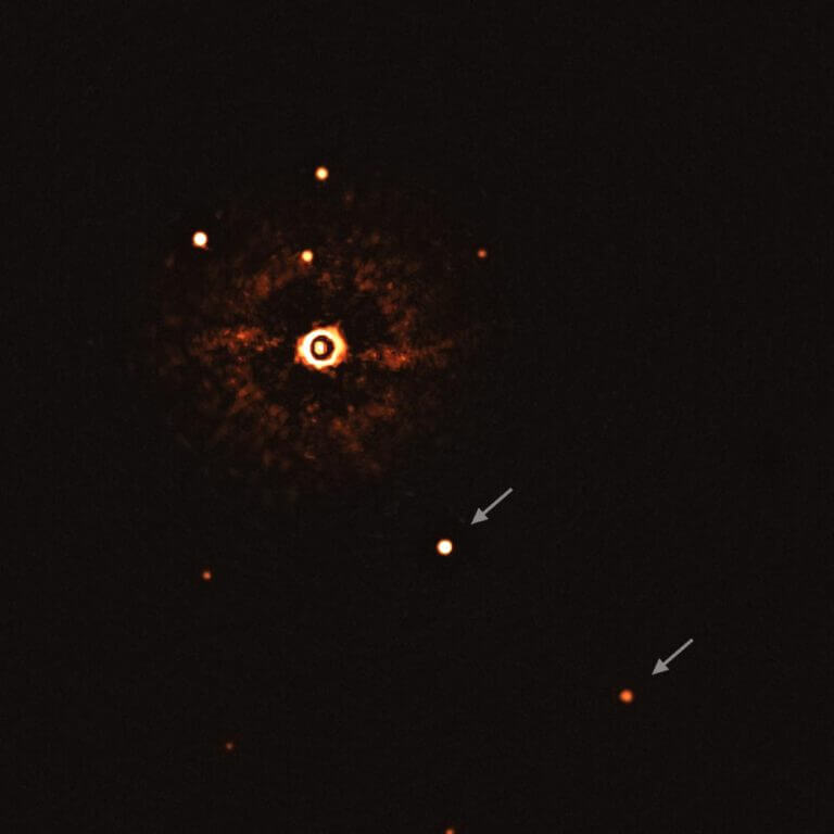 התמונה הזאת, שצולמה על ידי המכשיר SPHERE בטלסקופ הגדול מאוד של ESO, מראה את הכוכב TYC 8998-760-1 מלווה בשני כוכבי לכת חוץ שמשיים ענקיים, TYC 8998-760-1b ו-TYC 8998-760-1c. זאת הפעם הראשונה שאסטרונומים צפו ישירות ביותר מכוכב לכת אחד שמקיף כוכב הדומה לשמש. שני כוכבי הלכת נראים כשתי נקודות בהירות במרכז התמונה (TYC 8998-760-1b) ומימין למטה (TYC 8998-760-1c), מסומנים בחיצים. נקודות בהירות אחרות, שהן כוכבי רקע, נראות אף הן בתמונה. על ידי צילום של תמונות שונות בזמנים שונים, הצוות הצליח להבדיל בין כוכבי הלכת וכוכבי הרקע. התמונה צולמה על ידי חסימת האור מהכוכב הצעיר דמוי השמש (למעלה משמאל למרכז) באמצעות קורונוגרף, שמאפשר גילוי של כוכבי לכת חלשים יותר. הטבעות הבהירות וכהות שרואים על דמות הכוכב הן מכשירים אופטיים. מזכה: ESO/Bohn et al