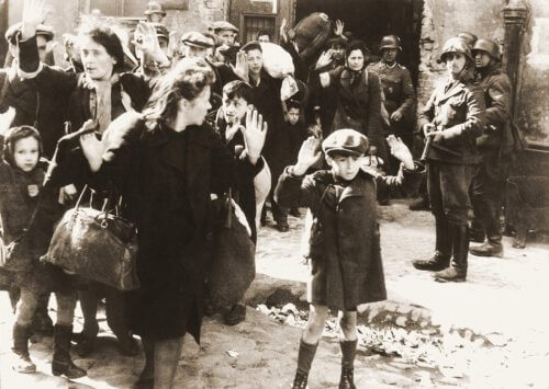 صبي يرفع يديه أثناء إخراج اليهود من المخابئ أثناء قمع الانتفاضة في وارسو عام 1943. تم التعرف على الصبي على أنه أرتور دومب سيمينتيك، أو إسرائيل روندل، أو تسفي نوسباوم، أو ليفي زيلينورجر. الأرشيف الفيدرالي الألماني / المجال العام