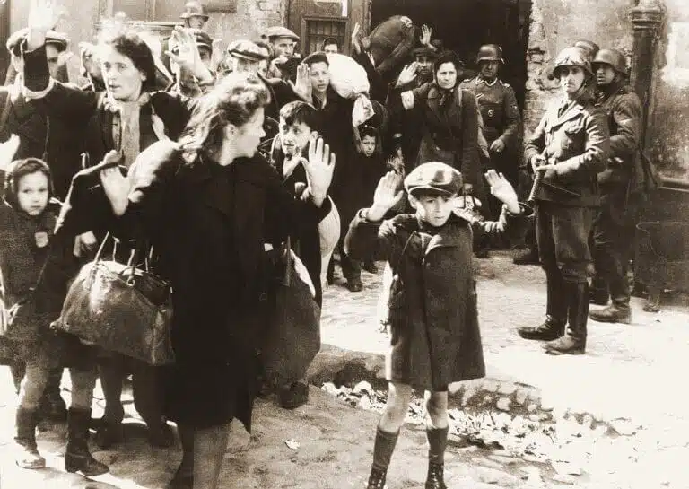 صبي يرفع يديه أثناء إخراج اليهود من المخابئ أثناء قمع الانتفاضة في وارسو عام 1943. تم التعرف على الصبي على أنه أرتور دومب سيمينتيك، أو إسرائيل روندل، أو تسفي نوسباوم، أو ليفي زيلينورجر. الأرشيف الفيدرالي الألماني / المجال العام