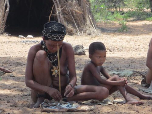 אישה משבט הקונג מכינה תכשיטים ליד ילד. סטהלר/ויקימדיה 