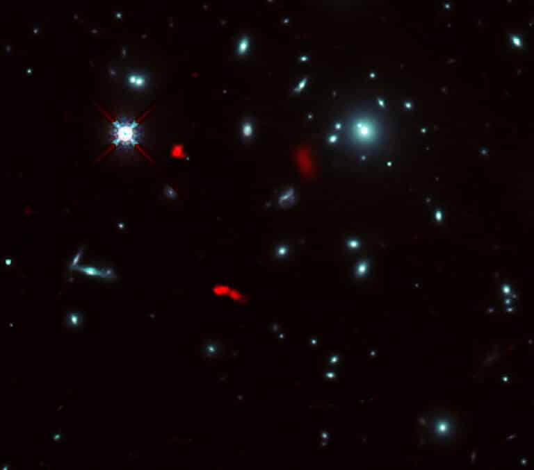 צביר הגלקסיות RXCJ0600-2007 שצולמה על ידי טלסקופ החלל האבל של נאס"א/ ESA, בשילוב עם תמונות עדשות כבידה של הגלקסיה הרחוקה RXCJ0600-z6, במרחק של 12.4 מיליארד שנות אור, שנצפו על ידי ALMA (מוצג באדום). בשל אפקט העדשה הכבידתית של צביר הגלקסיות, התמונה של RXCJ0600-z6 התעצמה והוגדלה, ונראה כי חולקה לשלושה חלקים או יותר. קרדיט: ALMA (ESO/NAOJ/NRAO), פוג'ימוטו ואח', טלסקופ החלל נאס"א/ESA האבל