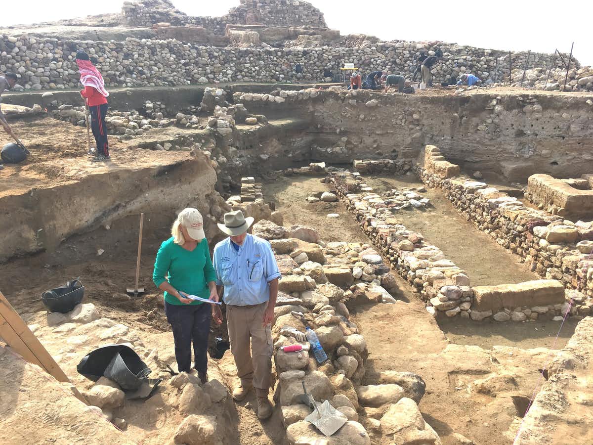 החוקרים עומדים ליד חורבות הקירות העתיקים, כאשר סימני שכבת ההרס נראים באמצע כל קיר חשוף. פיל סילביה, CC BY-ND