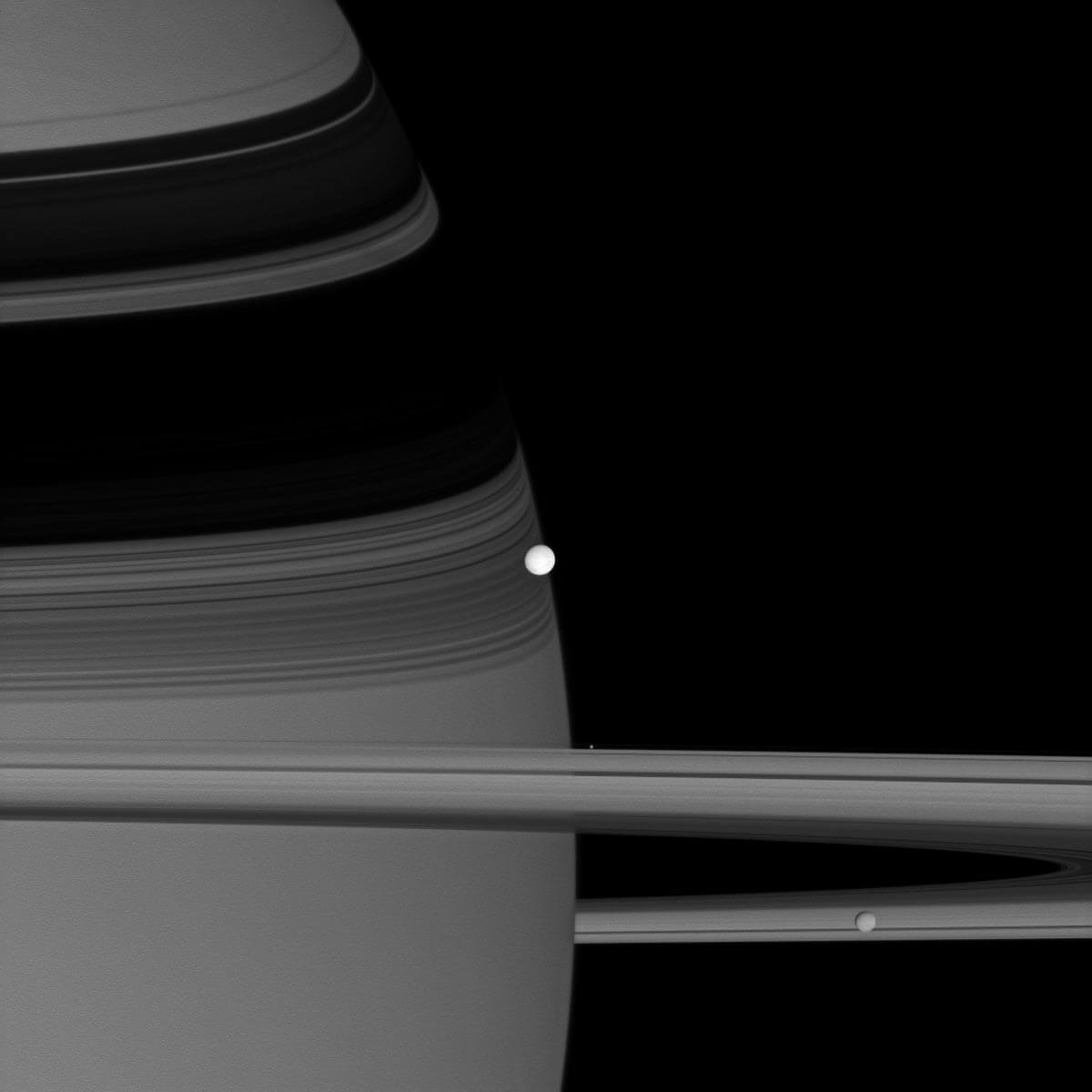 NASA's Cassini spacecraft captured this image of reflective Enceladus, seen in the center, as it orbits Saturn. Two other moons also appear in this image: Pandora, a bright blob hovering near the rings, and Mims, lower right.