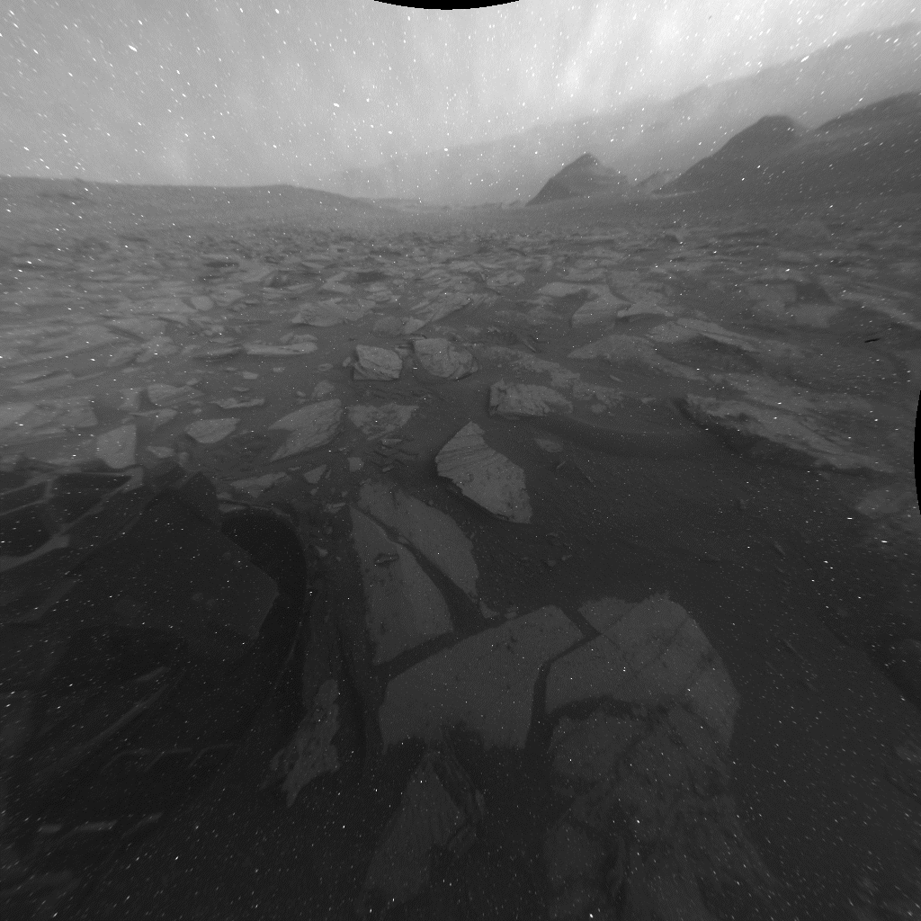 המצלמה האחורית Hazcam של סקרנות תיעדה את צל החלק האחורי של הרובר בתצפית של 12 שעות לכיוון רצפת אגן גייל. מספר גורמים גרמו למספר ארטיפקטים בתמונה, כולל נקודה שחורה, המראה המעוות של השמש, ושורות של פיקסלים לבנים הנמשכים מהשמש. נאס"א/JPL-Caltech