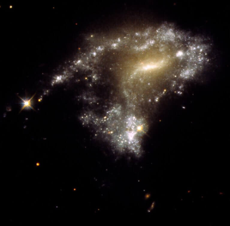 The galaxy AM 1054-325 has been warped from a normal pancake-like spiral shape into an S shape by the gravitational pull of a neighboring galaxy, as seen in this Hubble Space Telescope image. As a result, new star clusters were formed along a tidal tail stretched over thousands of light years, resembling a string of pearls. Credit: NASA, ESA, STScI, Jayanne English (University of Manitoba)