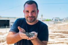 Archaeologist Shahar Crispin holds the hoard of coins after finding it. Photo by Yuli Schwartz
