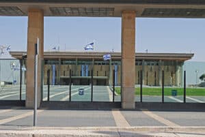 مبنى الكنيست الإسرائيلي يتميز بأعمدة حديثة وأعلام وطنية في ساحة مصممة.